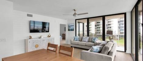 A modern living room with a wooden dining table, a sofa, and a TV mounted on the wall.