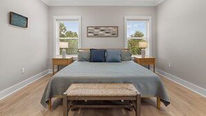 Um quarto com uma cama, duas mesas de cabeceira, um banco, um relógio de parede e uma janela com persianas.