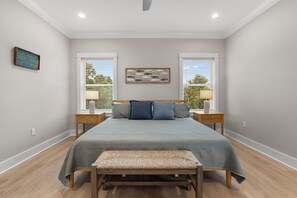 Un dormitorio con cama, dos mesitas de noche, un banco, un reloj de pared y una ventana con persianas.