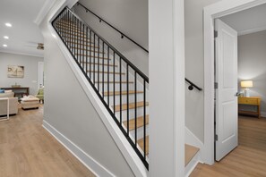 Una escalera con escalones de madera y barandillas negras, que conduce a una habitación con una puerta blanca y una lámpara sobre una mesita de noche de madera.