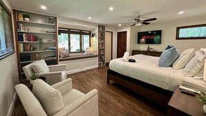 Un dormitorio con una cama, televisor, estantería, ventana y ventilador de techo.