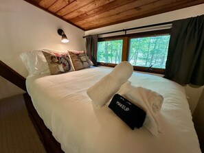 Una cama bien hecha con una almohada y una toalla, una lámpara de noche y una ventana con cortinas.
