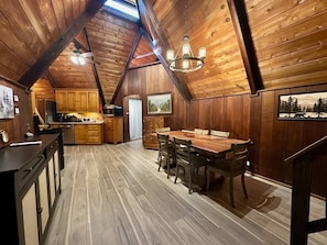 A log cabin interior with a dining area, kitchen, and a large window.