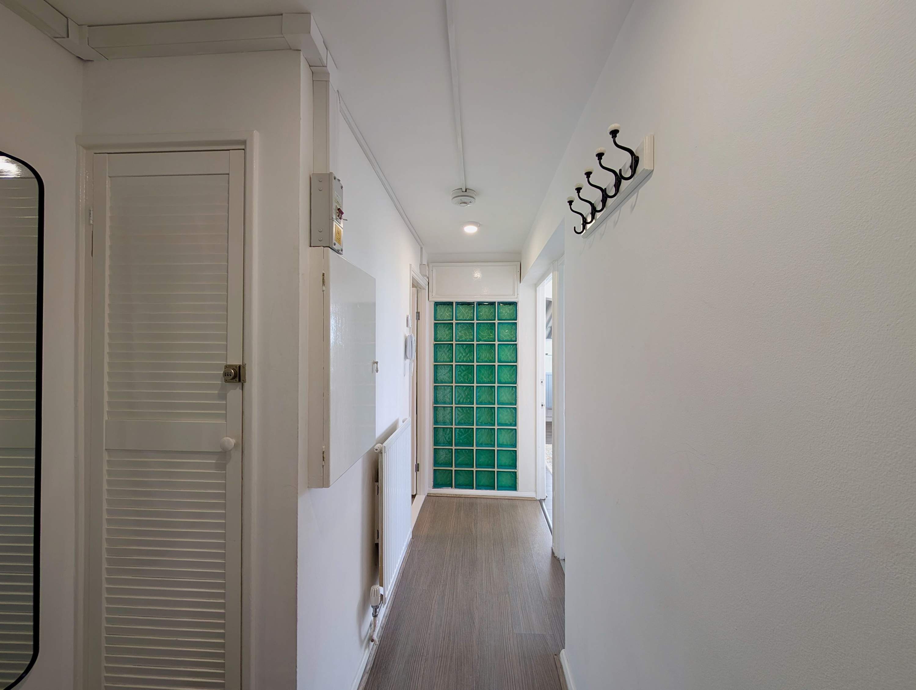 A hallway with a white door, a radiator, and a green glass door at the end.
