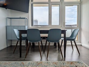Ein moderner Essbereich mit Tisch und Stühlen, einem grauen Schrank und einem großen Fenster mit Blick auf Gebäude.