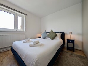 A neatly made bed with towels, a window, a bedside table with a lamp, and a nightstand. - 1bed Near Stratford with Breathtaking City Views (London)