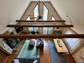 A loft-style room with a sloped ceiling, a fireplace, a sofa, a dining table, and a view through large windows.
