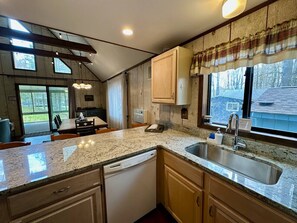 A kitchen with granite countertops, a dishwasher, wooden cabinets, a window with a view, and a dining area with a table and chairs.