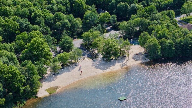 Vista aérea de uma área à beira de um lago, com vegetação densa e um pequeno cais que se projeta para a água.