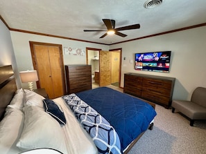 Ein Schlafzimmer mit Bett, Kommode, Fernseher und Deckenventilator.