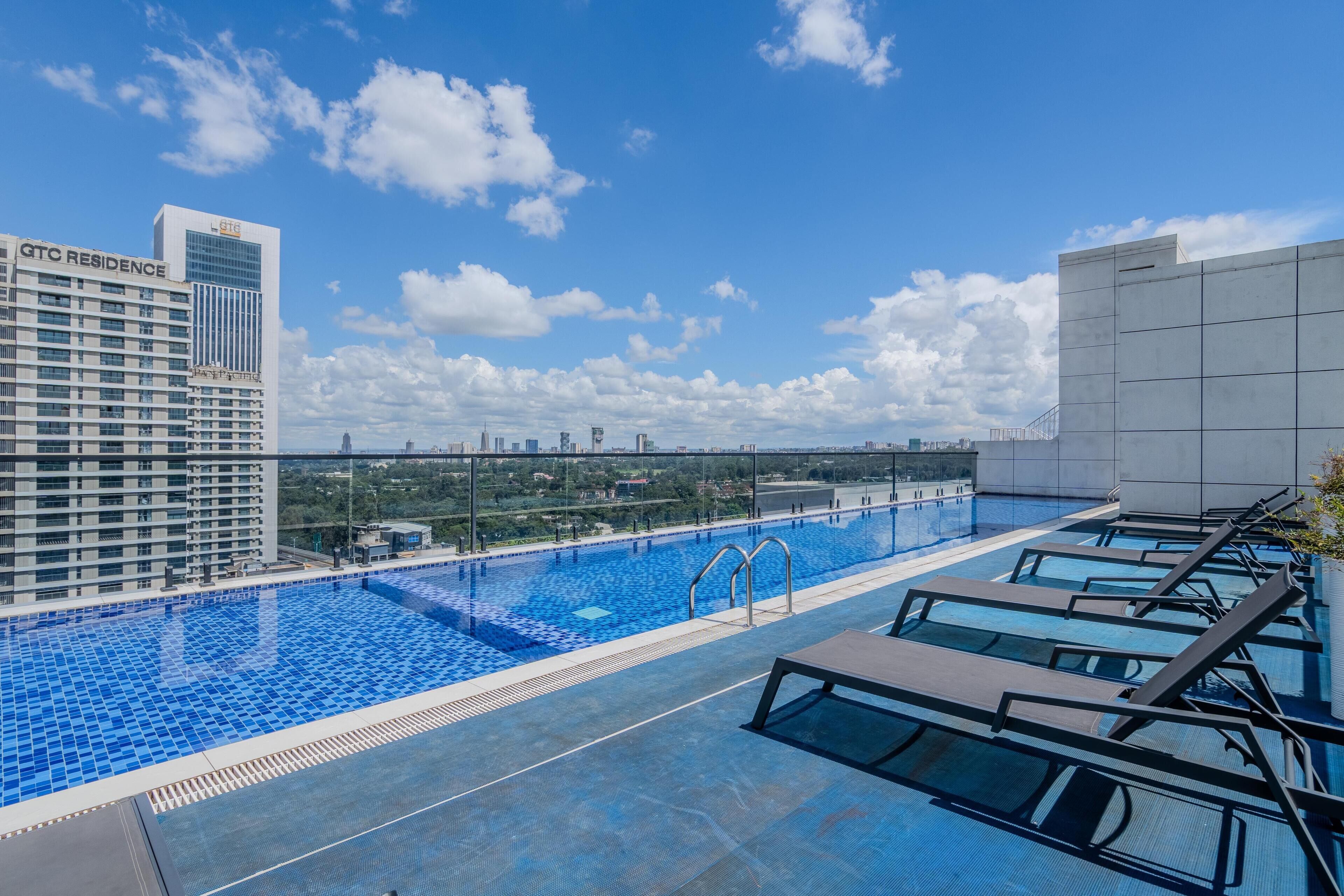 Una piscina infinita en la azotea con sillones de descanso y una vista despejada del horizonte de la ciudad, y el edificio GTC Residence.
