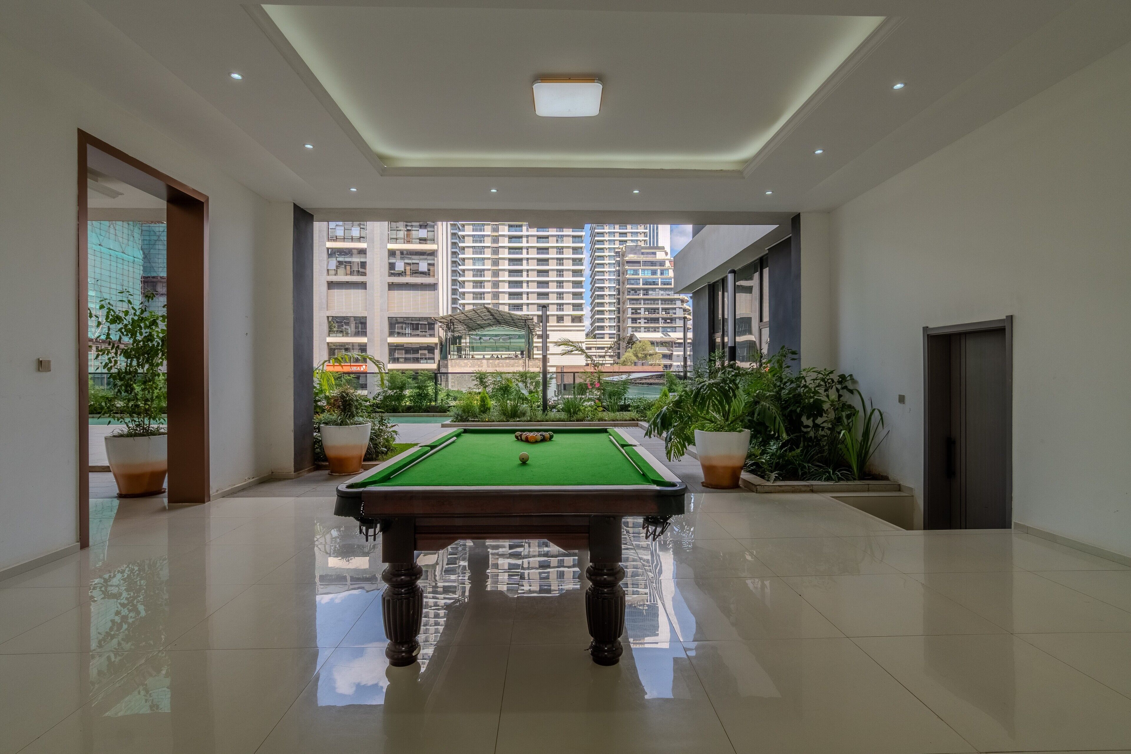 A pool table in a spacious room with a view of high-rise buildings and a covered outdoor area.