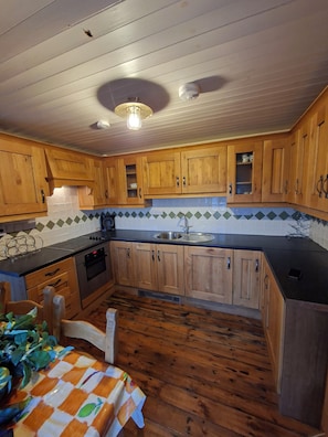 A kitchen with wooden cabinets, a black countertop, and a tiled backsplash. - The Atlantic on Your Doorstep. The Point by the Sea. Charming house in Carraroe (Carraroe)