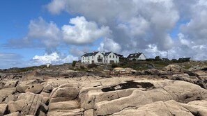 A coastal house with multiple rooms, a stone pathway, and a rocky foreground.