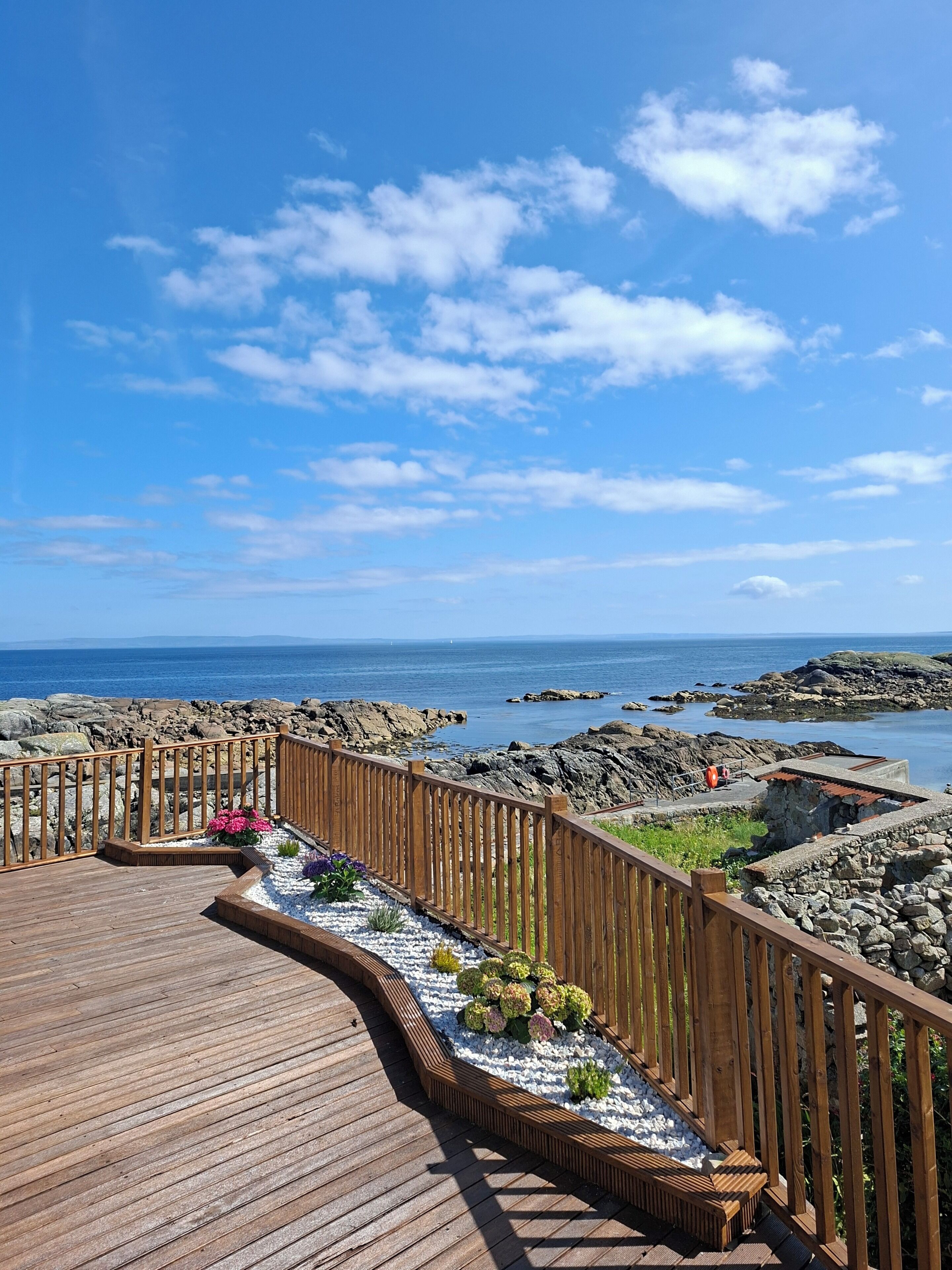 A wooden deck with a railing, overlooking a rocky coastline and the sea.