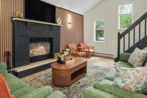 Una sala de estar con chimenea, sofás verdes, una mesa de centro y una escalera.