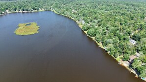 An aerial view of a lake surrounded by dense forest and a few scattered buildings. - Hot Tub ~ Luxury Landing (Tobyhanna)