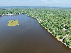 Vista aérea de un lago rodeado de bosque denso y algunas construcciones dispersas.