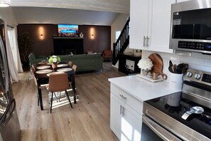 Eine moderne Küche mit Edelstahlgeräten, ein Essbereich mit Tisch und Stühlen sowie ein Wohnzimmer mit Sofa und Fernseher.