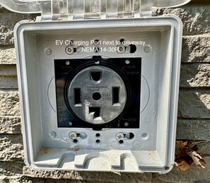 An EV charging port next to a driveway, with a NEMA 14-30R connector. - Romantic A-Frame - Hot Tub - Pets Welcome (Blakeslee)