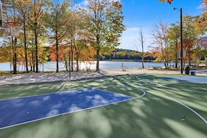 An outdoor basketball court with a green and blue surface, surrounded by trees with autumn foliage, a bench, and a picnic table. - Romantic A-Frame - Hot Tub - Pets Welcome (Blakeslee)