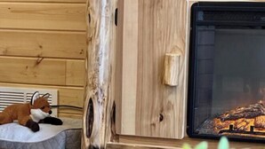 Une pièce chaleureuse avec un mur en bois, une cheminée, un confortable panier pour chien et une petite plante en pot.