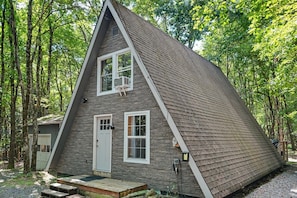 A triangular cabin with a stone facade, a front door, and a small porch. - Romantic A-Frame - Hot Tub - Pets Welcome (Blakeslee)