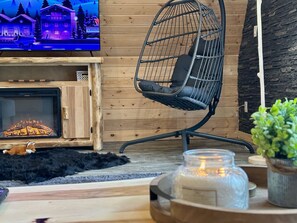 A cozy living room with a television, a fireplace, a hanging chair, and a small rug. - Romantic A-Frame - Hot Tub - Pets Welcome (Blakeslee)