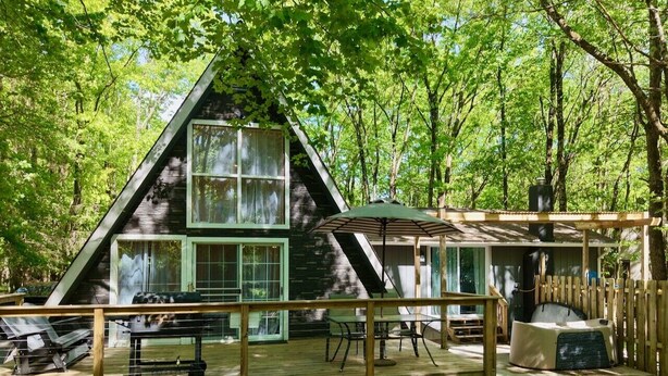 Une cabane dotée d’une terrasse, d’un espace extérieur couvert avec des sièges et d’une grande fenêtre.