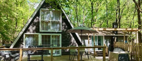 Une cabane dotée d’une terrasse, d’un espace extérieur couvert avec des sièges et d’une grande fenêtre.
