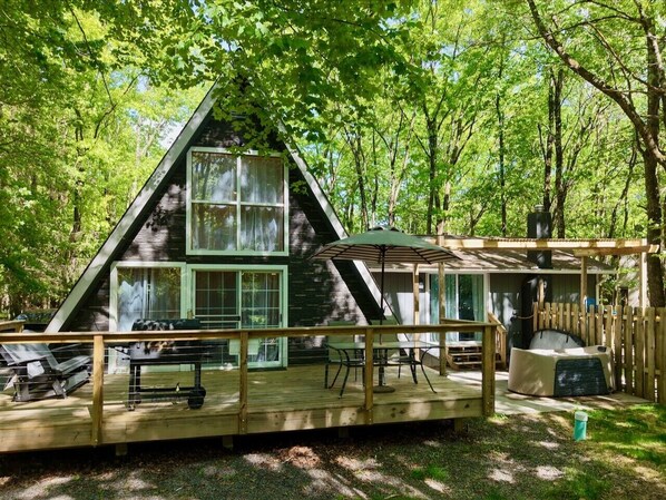A cabin with a deck, a covered outdoor seating area, and a large window. - Romantic A-Frame - Hot Tub - Pets Welcome (Blakeslee)