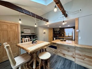 Ein Holzes Esstisch mit Hocker, eine Küche mit Steinrückwand und Pendelleuchten.