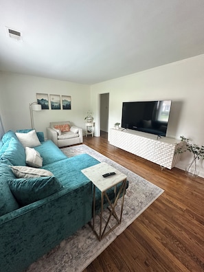 A living room with a teal sofa, a white coffee table, a TV, and a patterned rug. - Pet friendly High Point Terrace Gem-Backyard Oasis (Memphis)