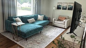 Un salon avec un canapé d’angle bleu, un fauteuil blanc, un téléviseur et une lampe sur pied.