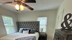 Ein Schlafzimmer mit Bett, Deckenventilator, Nachttisch, Kommode und Teppich.