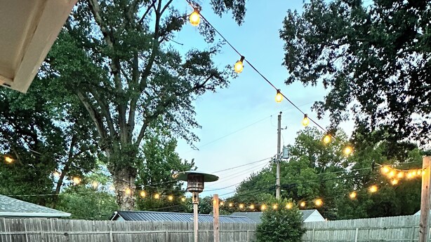 Une terrasse en bois, dotée de meubles d’extérieur, de guirlandes lumineuses et d’un barbecue.