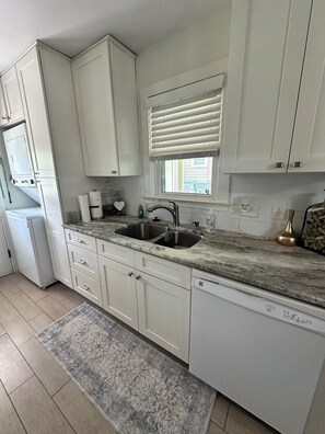 A kitchen with white cabinets, a double sink, a window with blinds, and a dishwasher.