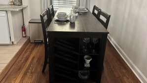 Un coin repas comprenant une table en bois, des chaises, un lustre et une fenêtre avec des stores.