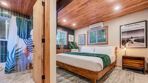 Een slaapkamer met een houten bedframe, een groene plaid, een nachtkastje en een ingelijste foto aan de muur.