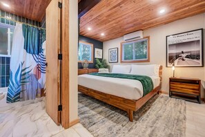 Une chambre à coucher avec un lit en bois, un plaid vert, une table de chevet et un tableau encadré accroché au mur.