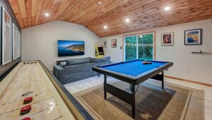 A pool table, a sofa, a television, and a scenic view through a glass door.