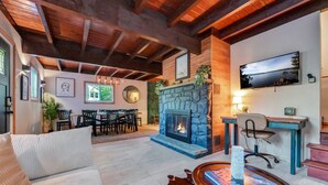 A cozy living room with a stone fireplace, a dining area, and a TV mounted on the wall.