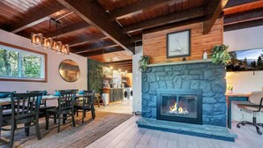 A modern kitchen with a stone fireplace, dining area with chairs, and a view of the outdoors.