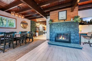 A modern kitchen with a stone fireplace, dining area with chairs, and a view of the outdoors. - Black Timber Chalet - Hot Tub - Game Room (Tobyhanna)