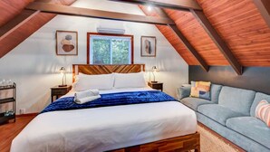 A bedroom with a sloped ceiling, a bed, a sofa, and two wall-mounted lamps.