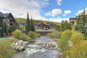 A river flowing through a lodge area with multiple buildings, a wooden bridge, and surrounding greenery. - Pet Friendly Hotel Room in Central Copper MTN! (Frisco)