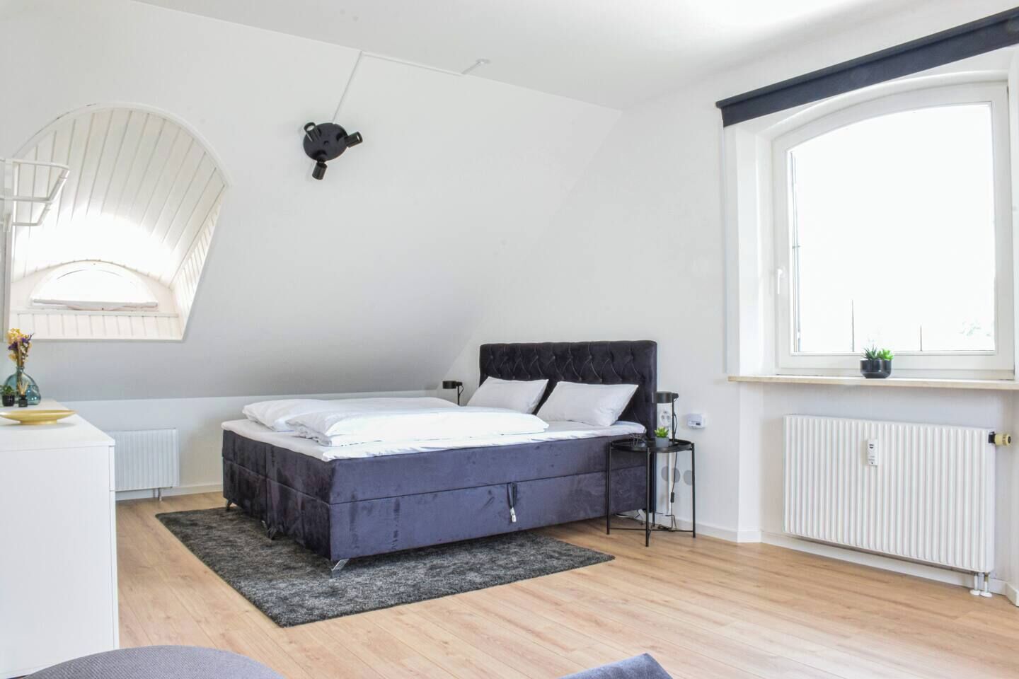 A modern bedroom with a bed, a small bedside table, a radiator, and a window.