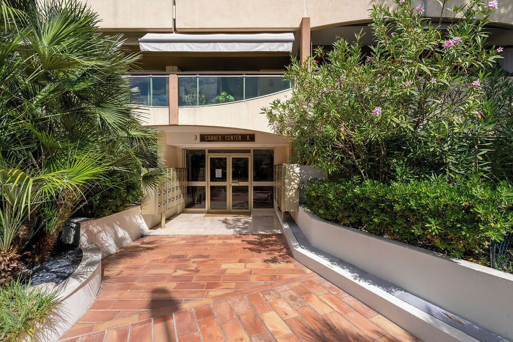A building entrance with a sign reading 'Cannes Center A,' surrounded by greenery and a tiled pathway.