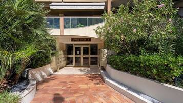 A building entrance with a sign reading 'Cannes Center A,' surrounded by greenery and a tiled pathway.