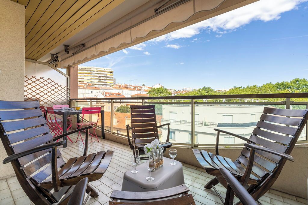 A balcony with wooden chairs, a table, and a vase with flowers.